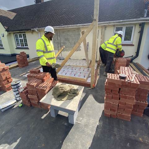 Bricklayers building a brick wall on a flat roof extension.