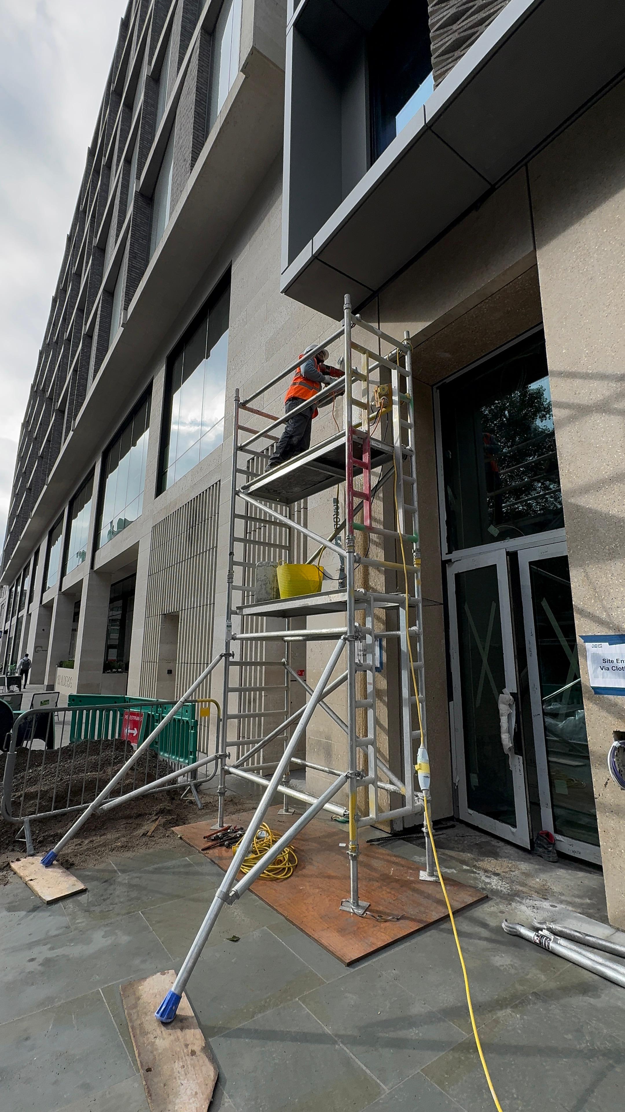 LCM Ltd operative working at height from a scaffold tower on a commercial building facade.